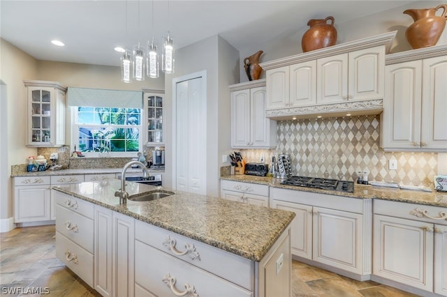 kitchen featuring decorative light fixtures, decorative backsplash, stainless steel gas cooktop, a kitchen island with sink, and sink