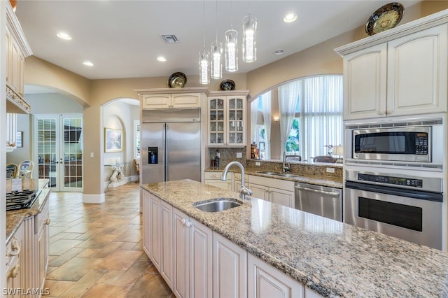 kitchen with sink, built in appliances, decorative light fixtures, and light stone countertops