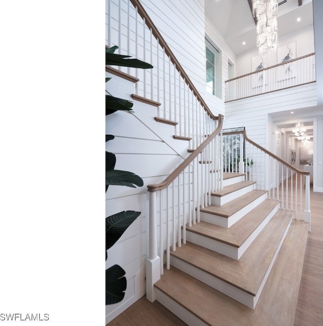 staircase with hardwood / wood-style floors, a notable chandelier, and a high ceiling