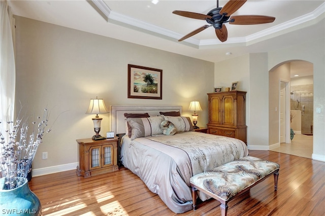 bedroom featuring connected bathroom, ceiling fan, a tray ceiling, and light hardwood / wood-style floors