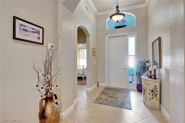 entryway featuring light tile patterned floors, ornamental molding, and a high ceiling