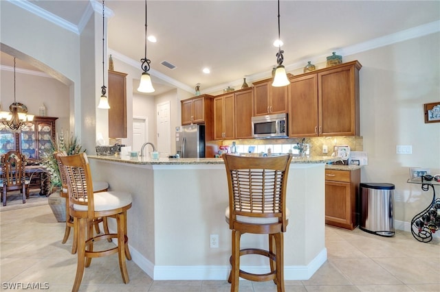 kitchen featuring pendant lighting, appliances with stainless steel finishes, light stone counters, and a breakfast bar area