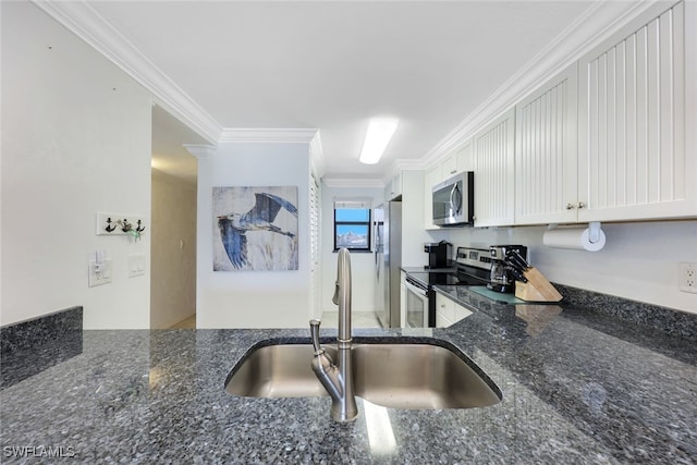 kitchen with dark stone countertops, ornamental molding, white cabinetry, stainless steel appliances, and sink