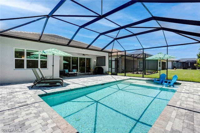 view of pool featuring a lawn, ceiling fan, a patio, and glass enclosure