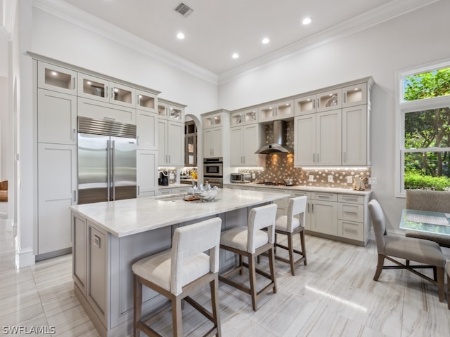 kitchen with wall chimney exhaust hood, a kitchen breakfast bar, light stone counters, a kitchen island, and appliances with stainless steel finishes