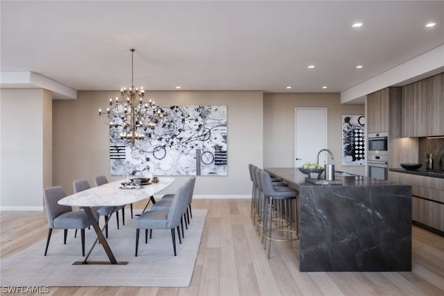 dining space with an inviting chandelier, sink, and light hardwood / wood-style flooring