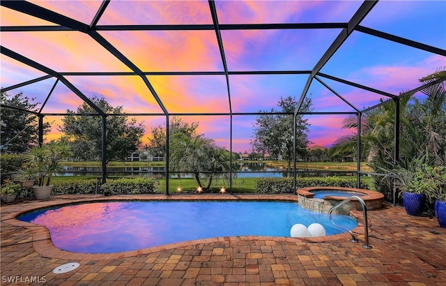 pool at dusk featuring an in ground hot tub, a water view, glass enclosure, and a patio area