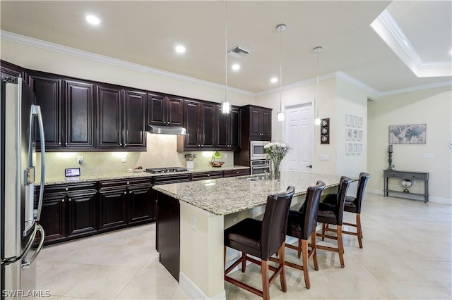 kitchen with a breakfast bar area, a kitchen island with sink, stainless steel appliances, light stone countertops, and decorative light fixtures