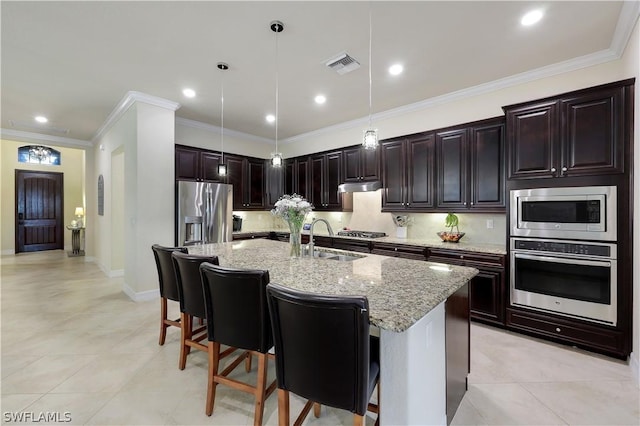 kitchen with a breakfast bar, sink, a center island with sink, appliances with stainless steel finishes, and pendant lighting