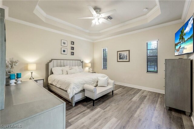 bedroom with wood-type flooring, a raised ceiling, and crown molding