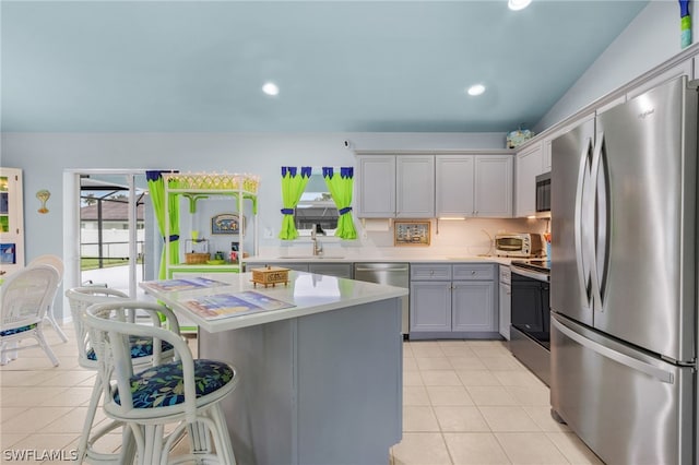 kitchen with appliances with stainless steel finishes, gray cabinets, vaulted ceiling, and light tile patterned flooring