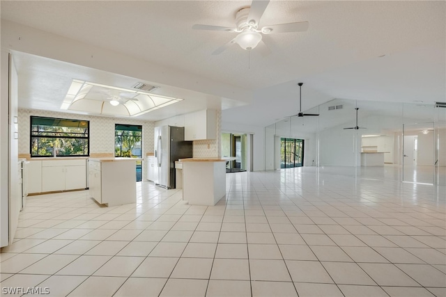 kitchen with stainless steel refrigerator, white cabinetry, a center island, lofted ceiling, and light tile patterned flooring