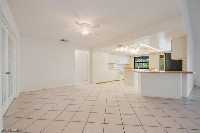 kitchen featuring kitchen peninsula, a textured ceiling, white appliances, and light tile patterned flooring