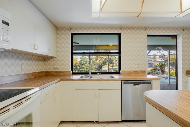 kitchen featuring white appliances, white cabinets, sink, light tile patterned floors, and butcher block counters