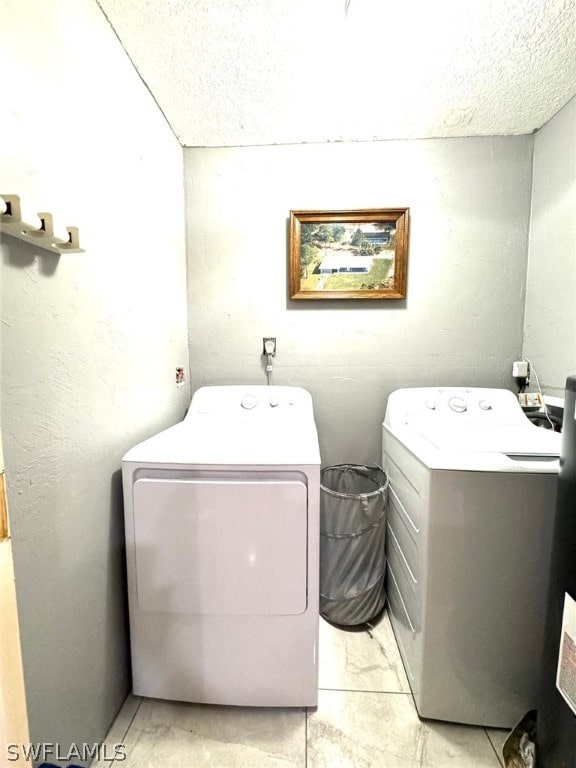 clothes washing area featuring light tile patterned flooring, washing machine and dryer, and a textured ceiling