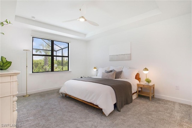 carpeted bedroom with ceiling fan and a raised ceiling