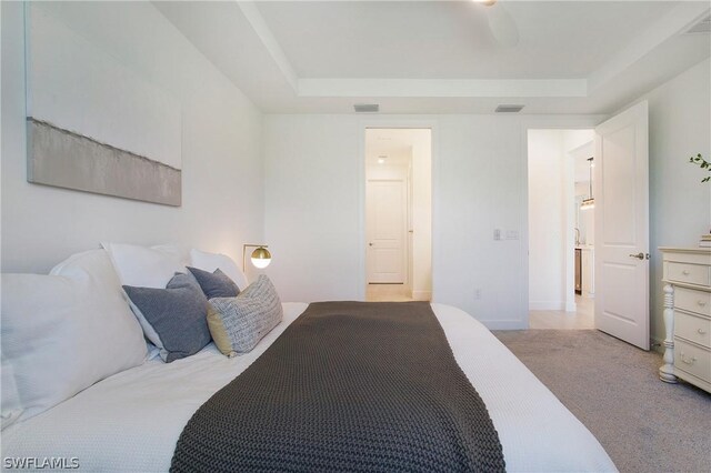 bedroom featuring light carpet, a raised ceiling, and ensuite bathroom