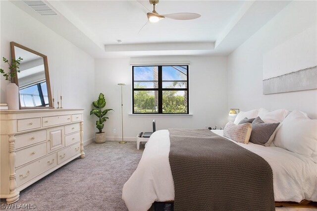 bedroom with multiple windows, a tray ceiling, light colored carpet, and ceiling fan