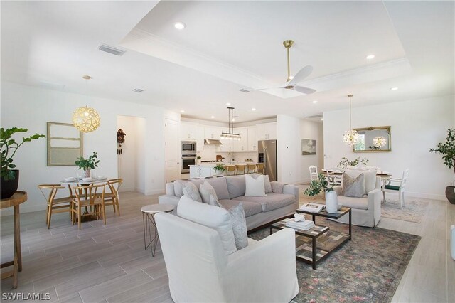 living room featuring a raised ceiling and ceiling fan with notable chandelier