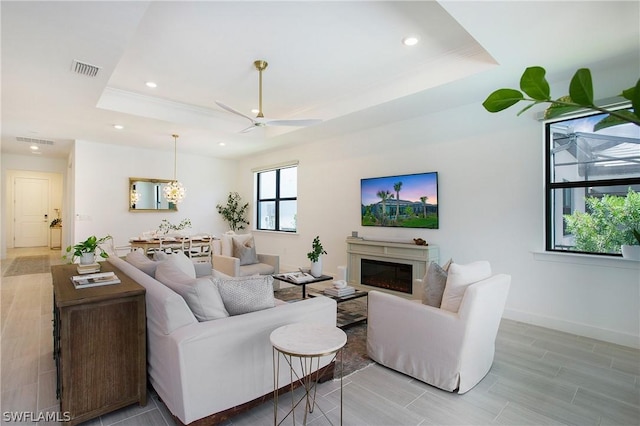 living room with a raised ceiling and ceiling fan with notable chandelier