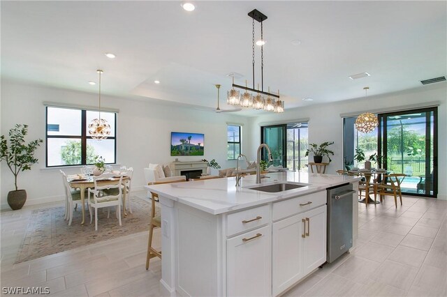 kitchen featuring sink, light stone counters, decorative light fixtures, an island with sink, and white cabinets