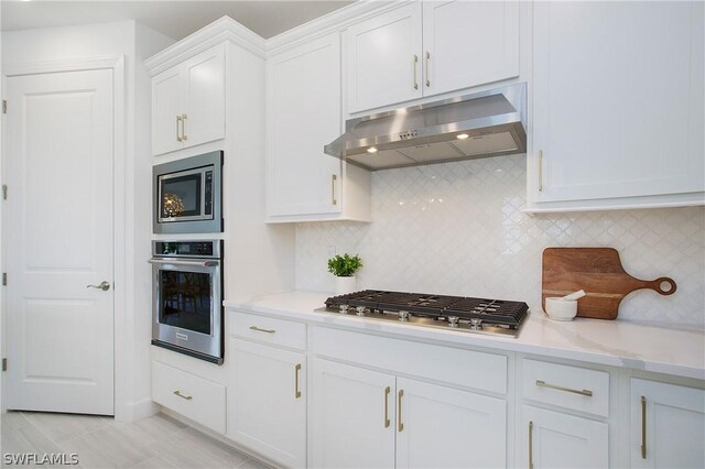 kitchen featuring appliances with stainless steel finishes, white cabinets, light stone counters, and decorative backsplash