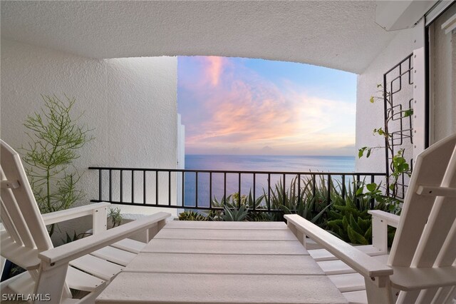 balcony at dusk featuring a water view