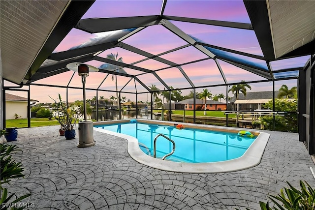 pool at dusk with glass enclosure, a water view, and a patio