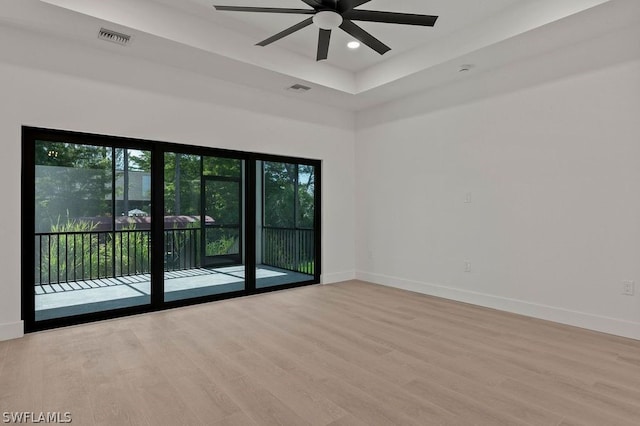 spare room with ceiling fan, light hardwood / wood-style floors, and a tray ceiling