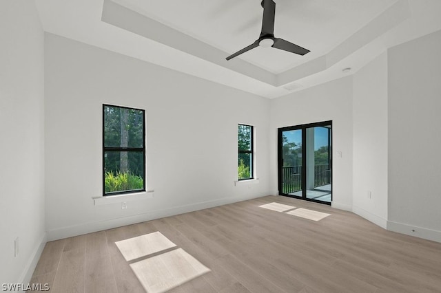 unfurnished room with light wood-type flooring, a raised ceiling, and ceiling fan