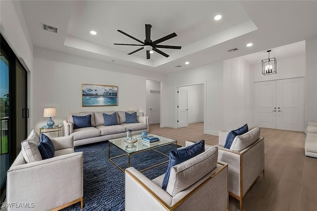 living room with ceiling fan with notable chandelier, a tray ceiling, and hardwood / wood-style flooring