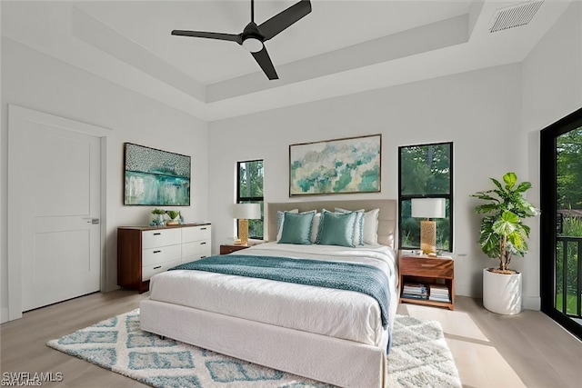 bedroom featuring ceiling fan, light hardwood / wood-style floors, a towering ceiling, and a tray ceiling