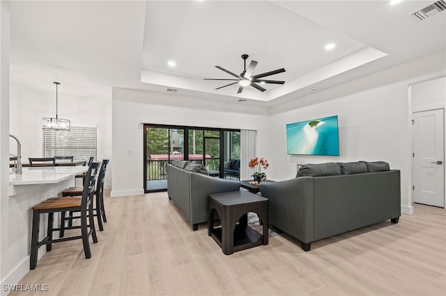 27071 Holly Ln, Bonita Springs, FL 34135 - living room with ceiling fan with notable chandelier, a tray ceiling, visible vents, and light wood-style floors
