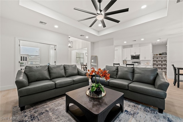 living room featuring a tray ceiling, light wood-type flooring, visible vents, and recessed lighting