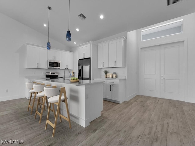 kitchen featuring white cabinets, stainless steel appliances, a kitchen island with sink, and vaulted ceiling