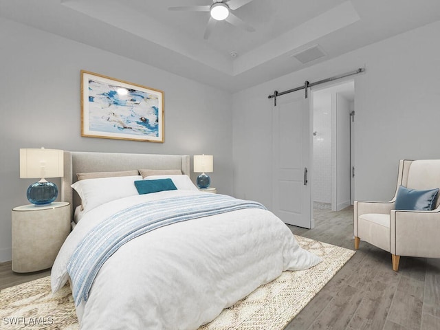 bedroom featuring wood-type flooring, a barn door, a tray ceiling, and ceiling fan