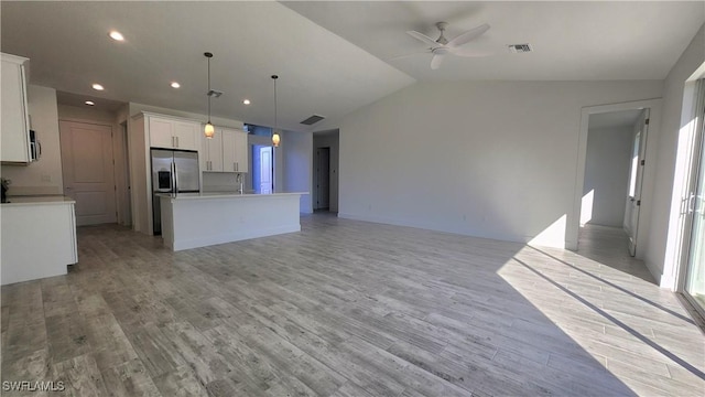 kitchen with pendant lighting, lofted ceiling, a kitchen island with sink, white cabinets, and light wood-type flooring