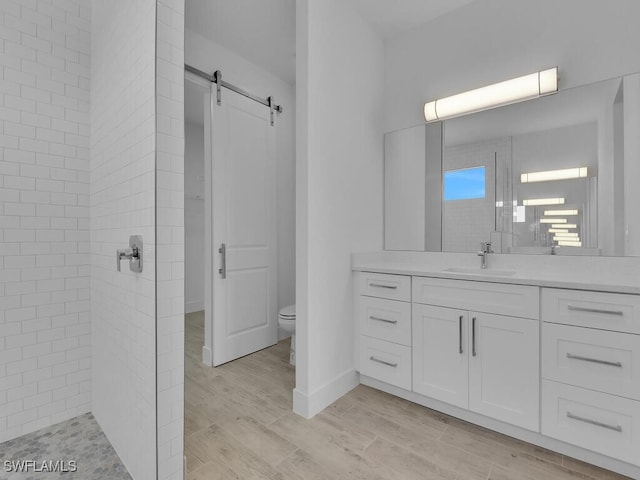 bathroom with tiled shower, hardwood / wood-style floors, toilet, and vanity