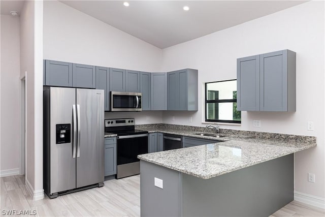 kitchen with light stone countertops, stainless steel appliances, kitchen peninsula, and sink