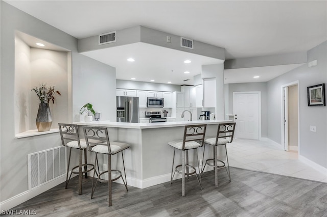 kitchen featuring white cabinetry, stainless steel appliances, kitchen peninsula, wood-type flooring, and a breakfast bar