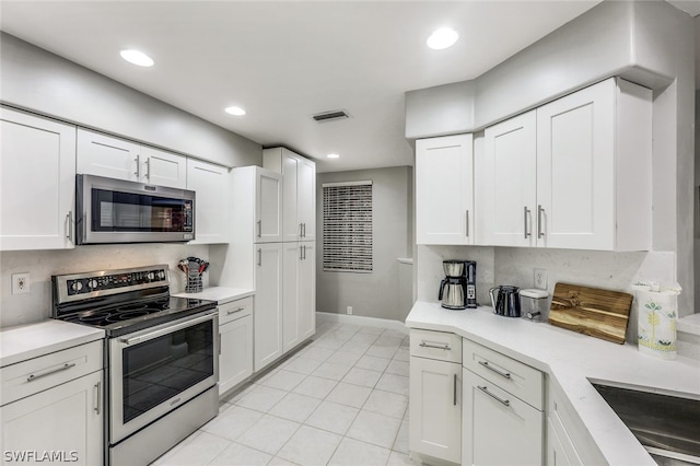 kitchen with white cabinets, light tile patterned floors, appliances with stainless steel finishes, and tasteful backsplash