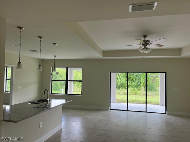 kitchen featuring a raised ceiling, light stone countertops, ceiling fan, sink, and decorative light fixtures