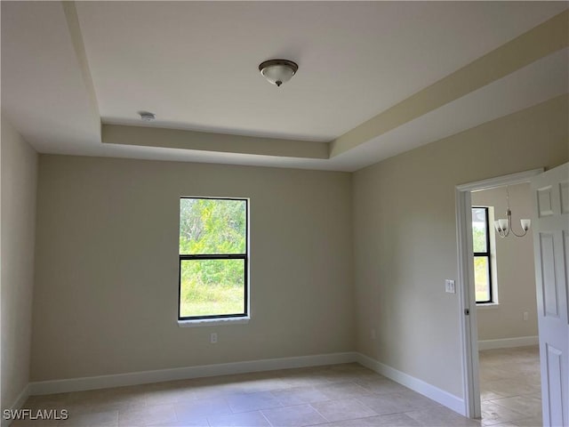 empty room featuring a raised ceiling, light tile patterned floors, and a chandelier