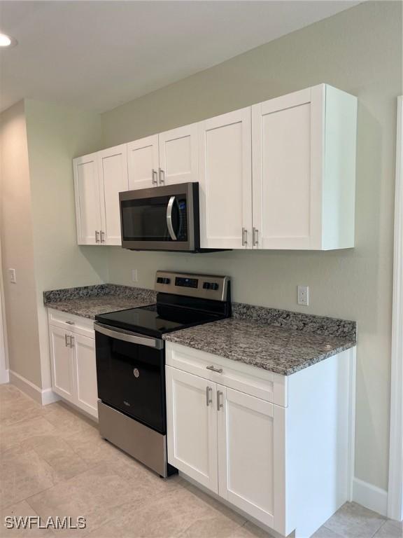 kitchen with white cabinets, light tile patterned flooring, dark stone countertops, and appliances with stainless steel finishes