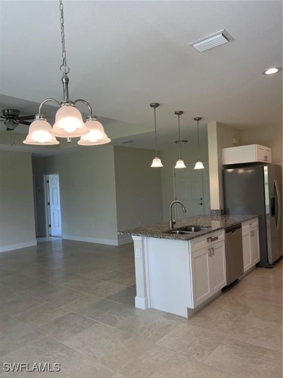 kitchen with dark stone countertops, appliances with stainless steel finishes, white cabinets, decorative light fixtures, and sink