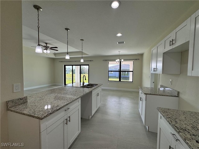 kitchen with sink, decorative light fixtures, white cabinetry, ceiling fan with notable chandelier, and a kitchen island