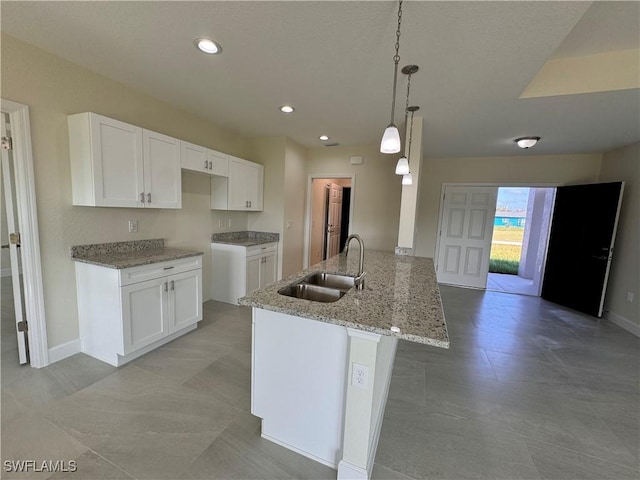 kitchen with sink, white cabinetry, kitchen peninsula, hanging light fixtures, and light stone countertops