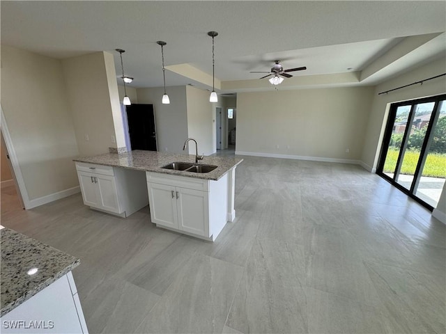 kitchen with sink, white cabinetry, pendant lighting, light stone countertops, and a tray ceiling