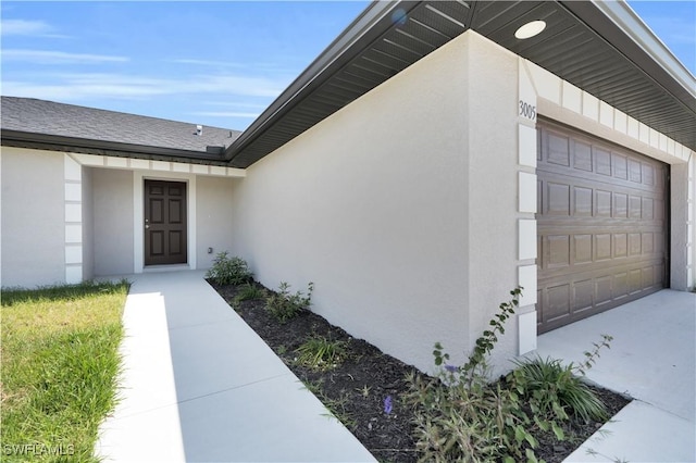 view of exterior entry featuring stucco siding and roof with shingles