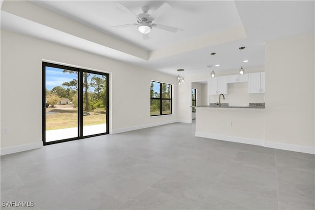 unfurnished living room featuring a raised ceiling, ceiling fan, baseboards, and a sink